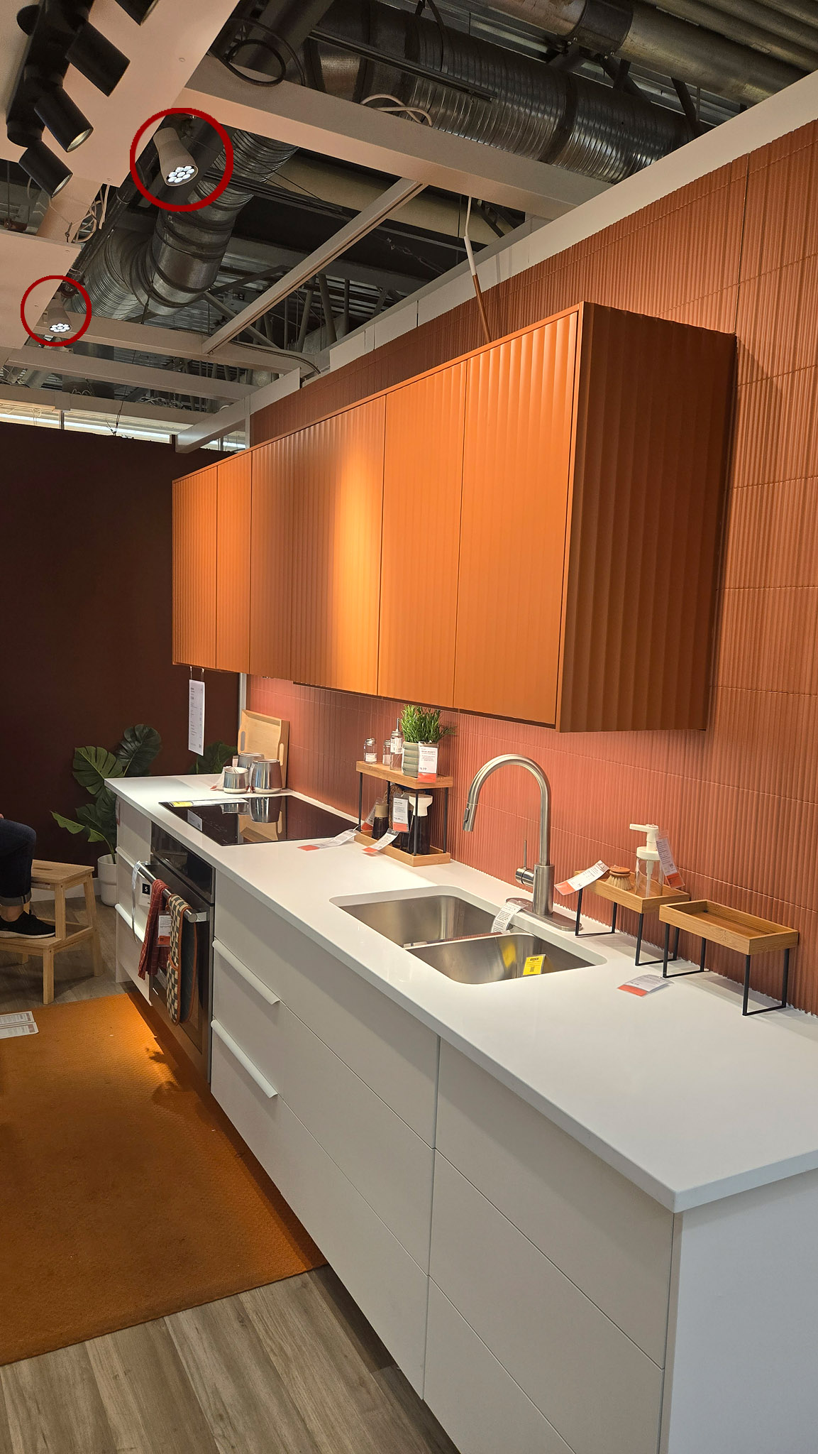 Terracotta IKEA kitchen display with two small spotlights circled in red on the ceiling grid above